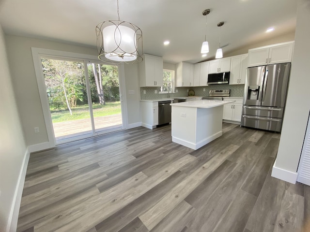 kitchen with white cabinets, appliances with stainless steel finishes, a center island, and decorative light fixtures