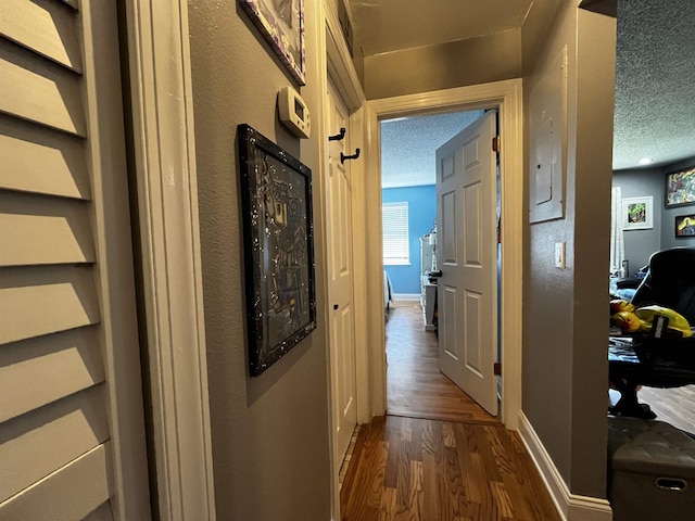 corridor with a textured ceiling and dark hardwood / wood-style flooring