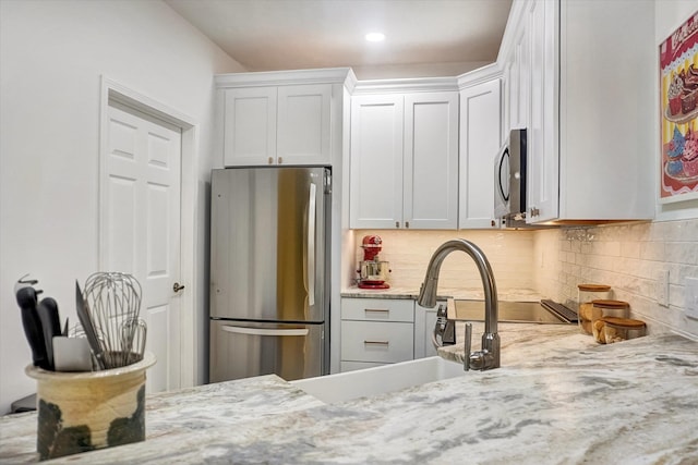 kitchen featuring white cabinets, light stone countertops, stainless steel appliances, and tasteful backsplash