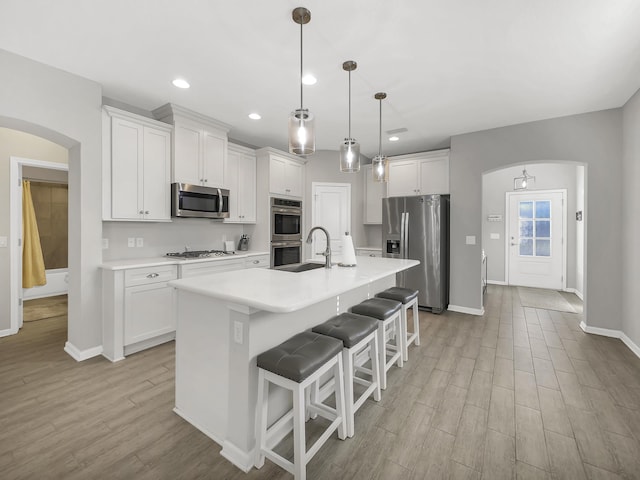55 Concave Ln, Saint Augustine, FL 32095 - kitchen with arched walkways, stainless steel appliances, light wood finished floors, white cabinets, and a sink