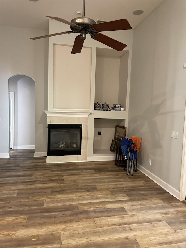 unfurnished living room with a tiled fireplace, hardwood / wood-style flooring, and ceiling fan