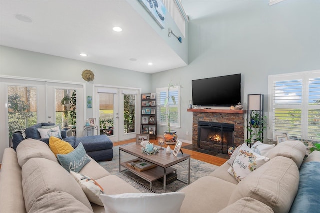 living room with a stone fireplace, light wood-type flooring, a high ceiling, and french doors