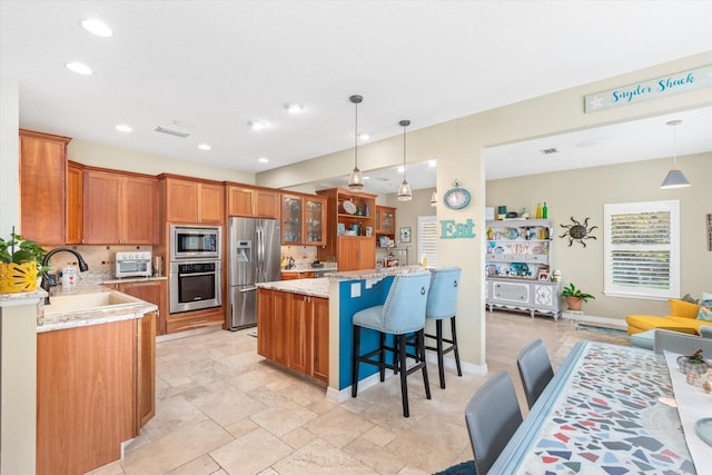 kitchen featuring light stone counters, a breakfast bar, stainless steel appliances, sink, and pendant lighting