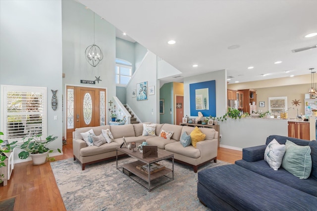 living room with a healthy amount of sunlight, wood-type flooring, a towering ceiling, and an inviting chandelier