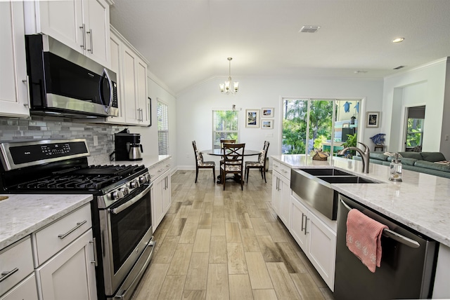 kitchen with hanging light fixtures, vaulted ceiling, appliances with stainless steel finishes, white cabinetry, and a chandelier