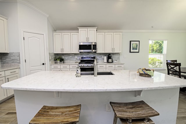 kitchen with crown molding, white cabinetry, a kitchen island with sink, and appliances with stainless steel finishes