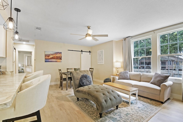 living area featuring a barn door, light wood-type flooring, ceiling fan, and baseboards