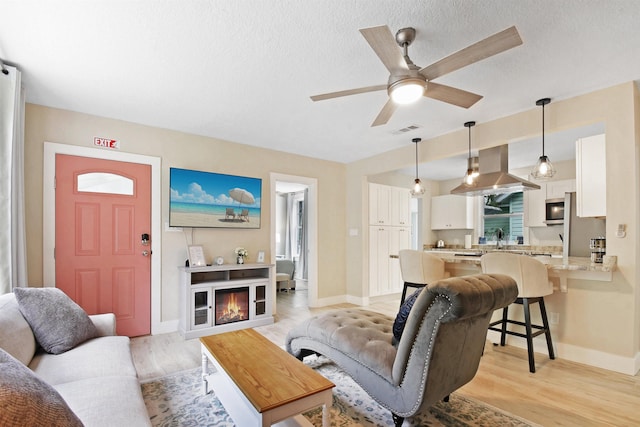living area featuring baseboards, a ceiling fan, light wood-style flooring, and a textured ceiling