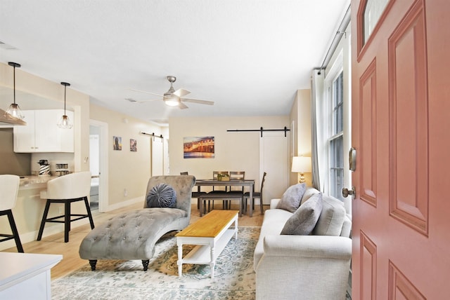 living area featuring a barn door, light wood-style floors, a ceiling fan, and baseboards