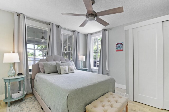 bedroom with a textured ceiling, light wood-style floors, baseboards, and a ceiling fan