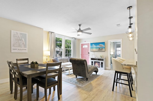 dining room featuring a ceiling fan, light wood-style flooring, baseboards, and a glass covered fireplace