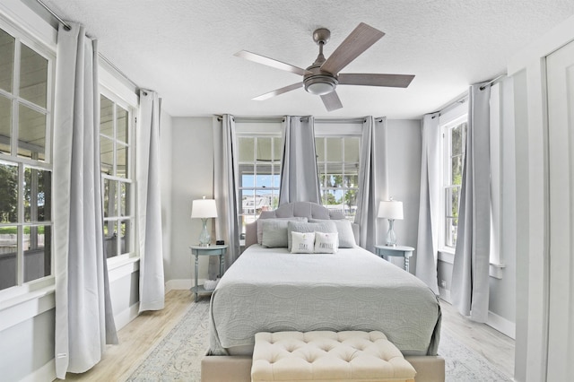 bedroom featuring light wood finished floors, a textured ceiling, baseboards, and ceiling fan
