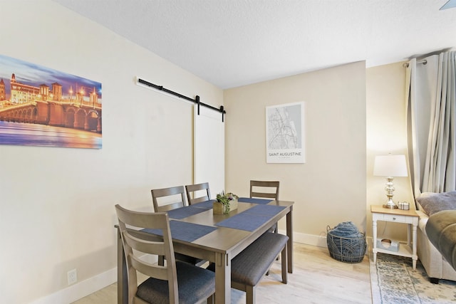dining area with a barn door, light wood-style floors, baseboards, and a textured ceiling