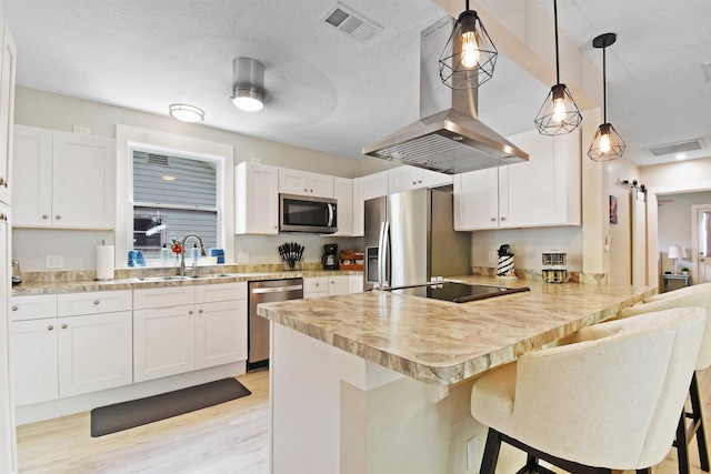 kitchen featuring stainless steel appliances, a sink, wall chimney exhaust hood, a peninsula, and light countertops