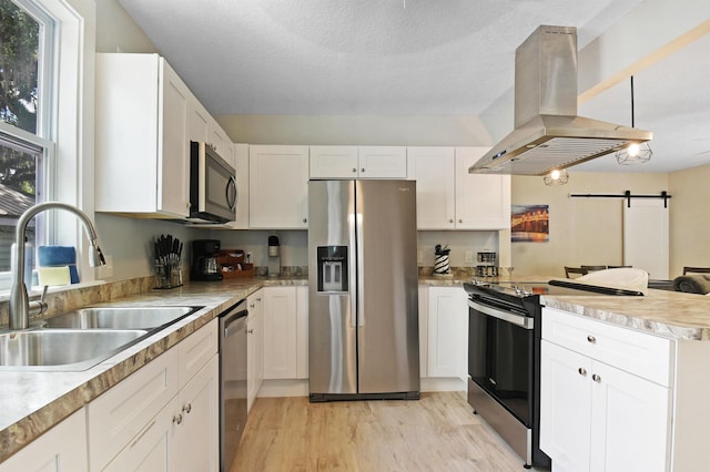 kitchen featuring stainless steel appliances, a sink, island exhaust hood, a peninsula, and light wood-style flooring
