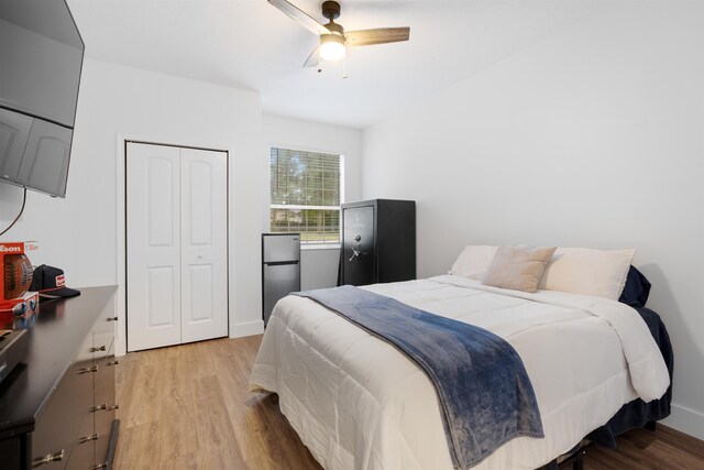 bedroom featuring stainless steel fridge, light wood-type flooring, a closet, and ceiling fan