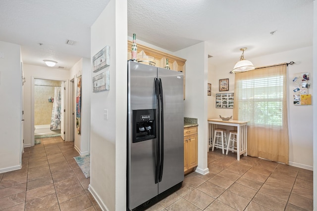 kitchen with stainless steel refrigerator with ice dispenser, a textured ceiling, light tile patterned floors, and light brown cabinetry