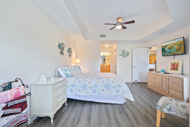 bedroom featuring hardwood / wood-style floors, a tray ceiling, ceiling fan, and ensuite bathroom