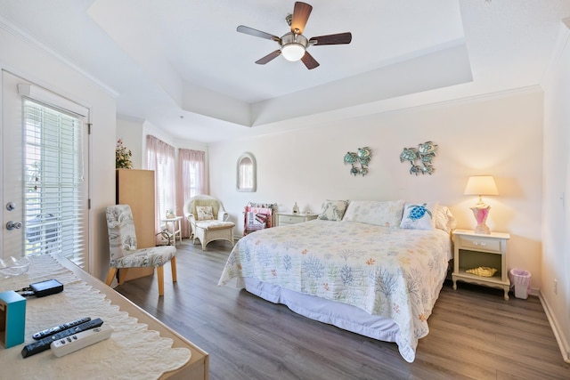 bedroom with dark hardwood / wood-style flooring, a tray ceiling, multiple windows, and ceiling fan