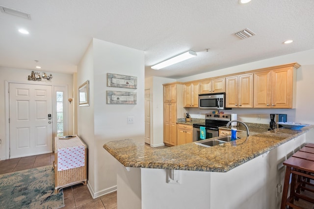 kitchen featuring kitchen peninsula, light brown cabinetry, a breakfast bar, stainless steel appliances, and sink