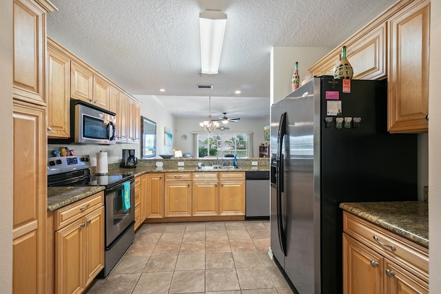 kitchen with kitchen peninsula, dark stone countertops, light tile patterned floors, ceiling fan with notable chandelier, and appliances with stainless steel finishes