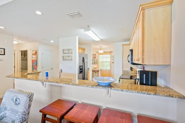 kitchen featuring kitchen peninsula, stainless steel fridge with ice dispenser, light brown cabinets, and light stone countertops