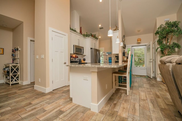 kitchen with appliances with stainless steel finishes, white cabinetry, a kitchen breakfast bar, hanging light fixtures, and kitchen peninsula