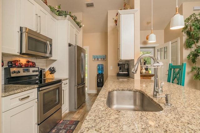 kitchen with stainless steel appliances, sink, white cabinetry, and decorative light fixtures