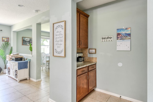 104 Claremont Ct, Elkton, FL 32033 - kitchen featuring light tile patterned floors, a textured ceiling, brown cabinetry, tasteful backsplash, and light stone countertops