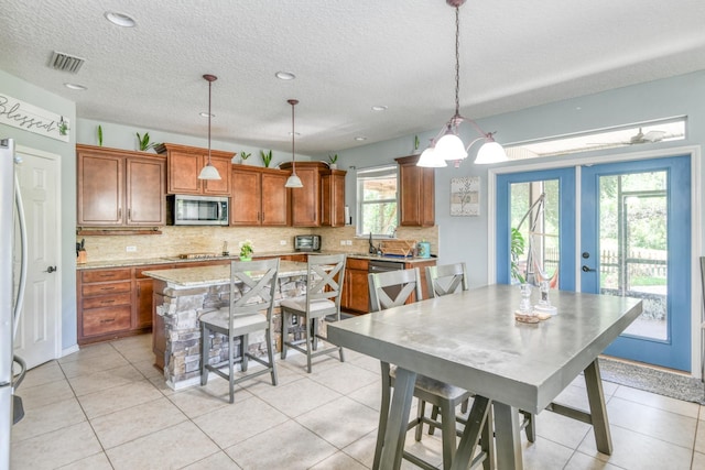 104 Claremont Ct, Elkton, FL 32033 - kitchen with stainless steel appliances, backsplash, brown cabinetry, light tile patterned floors, and a textured ceiling