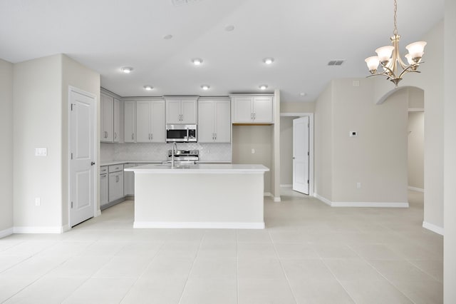 kitchen featuring sink, backsplash, hanging light fixtures, a kitchen island with sink, and light tile patterned floors