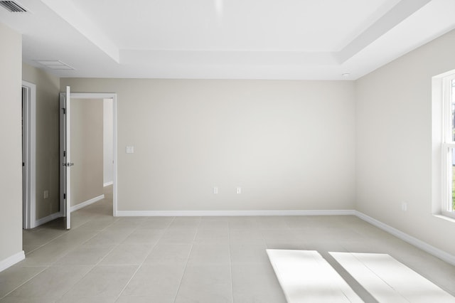 spare room with plenty of natural light, a tray ceiling, and light tile patterned floors