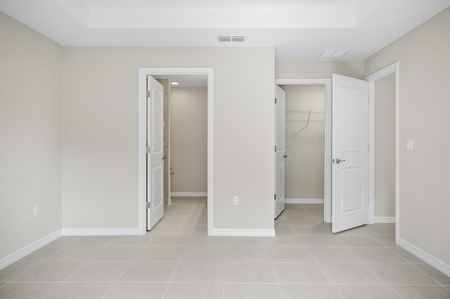 unfurnished bedroom featuring a closet, a walk in closet, light tile patterned floors, and a tray ceiling