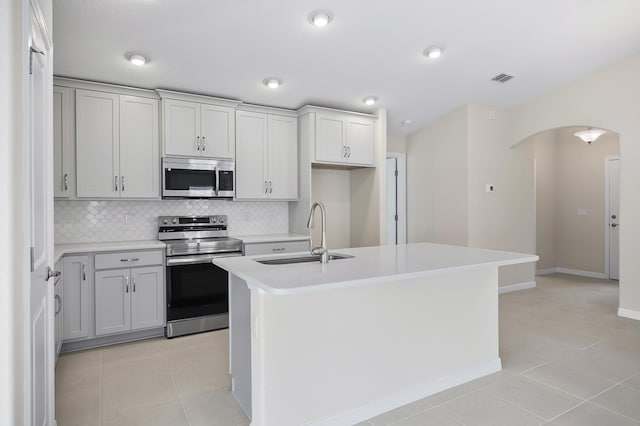 kitchen featuring appliances with stainless steel finishes, an island with sink, sink, backsplash, and light tile patterned floors