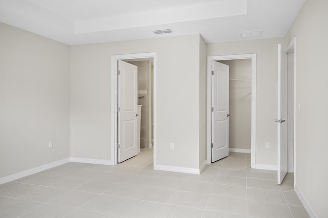 unfurnished bedroom featuring connected bathroom, a spacious closet, light tile patterned floors, a raised ceiling, and a closet