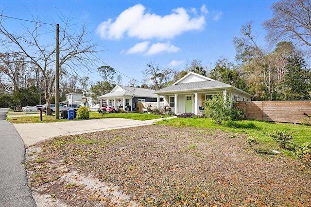 view of front facade with a porch, concrete driveway, fence, and a shingled roof