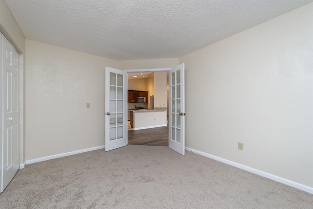 empty room featuring light carpet, french doors, and a textured ceiling