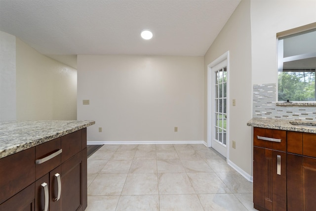 unfurnished dining area with a textured ceiling, lofted ceiling, sink, and light tile patterned floors