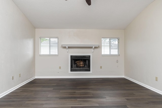 unfurnished living room featuring a wealth of natural light, ceiling fan, dark wood-type flooring, and a textured ceiling