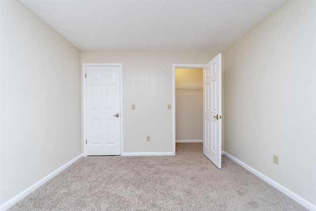 unfurnished bedroom featuring a spacious closet, light colored carpet, and a textured ceiling