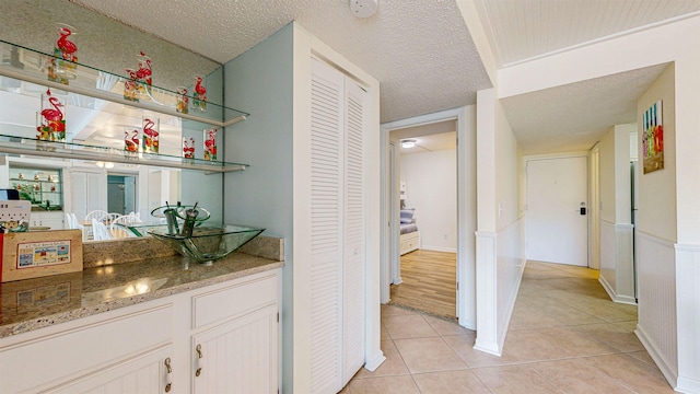 bar with white cabinetry, light tile patterned flooring, stone countertops, and a textured ceiling