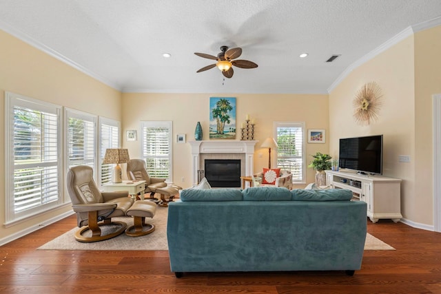 living room featuring crown molding, a textured ceiling, dark hardwood / wood-style floors, ceiling fan, and a tiled fireplace