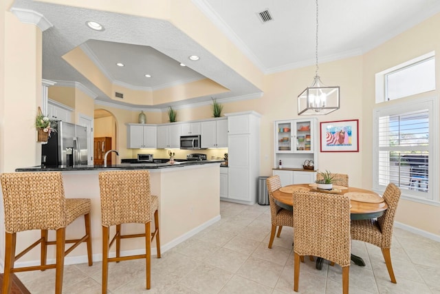 kitchen with stainless steel appliances, a raised ceiling, white cabinets, and kitchen peninsula