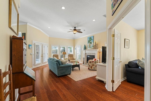 living room with dark hardwood / wood-style floors, a fireplace, ornamental molding, ceiling fan, and a textured ceiling