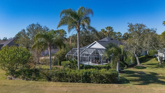 rear view of property with glass enclosure and a lawn