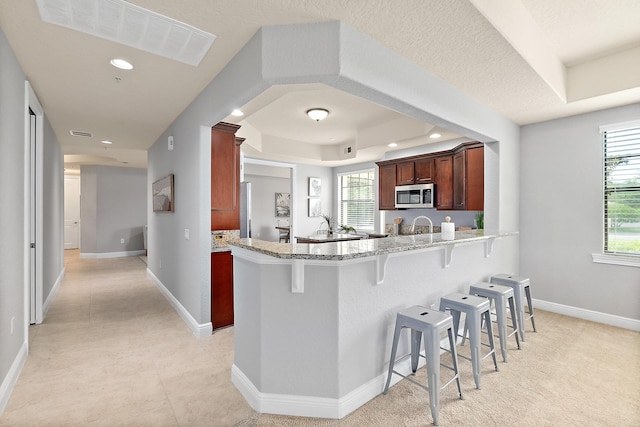 175 Laterra Links Cir Unit 101, Saint Augustine, FL 32092 - kitchen with stainless steel microwave, a peninsula, a breakfast bar area, visible vents, and light stone countertops
