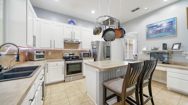 kitchen with visible vents, under cabinet range hood, a sink, stainless steel appliances, and arched walkways