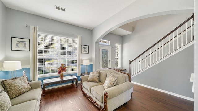 living room with visible vents, hardwood / wood-style flooring, arched walkways, baseboards, and stairs