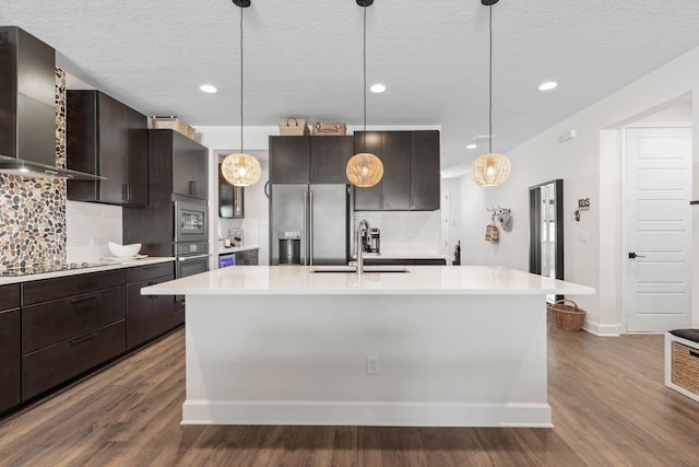 kitchen featuring a sink, light countertops, wall chimney range hood, appliances with stainless steel finishes, and dark wood finished floors