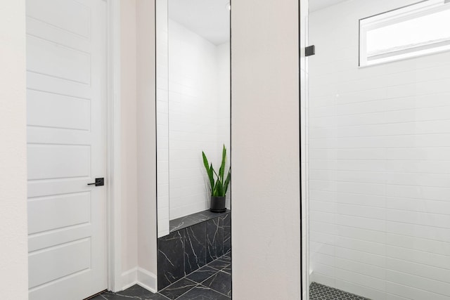 bathroom with marble finish floor, a tile shower, and baseboards